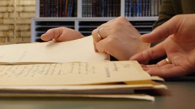 Screenshot from the movie. Hands of two people go through old documents