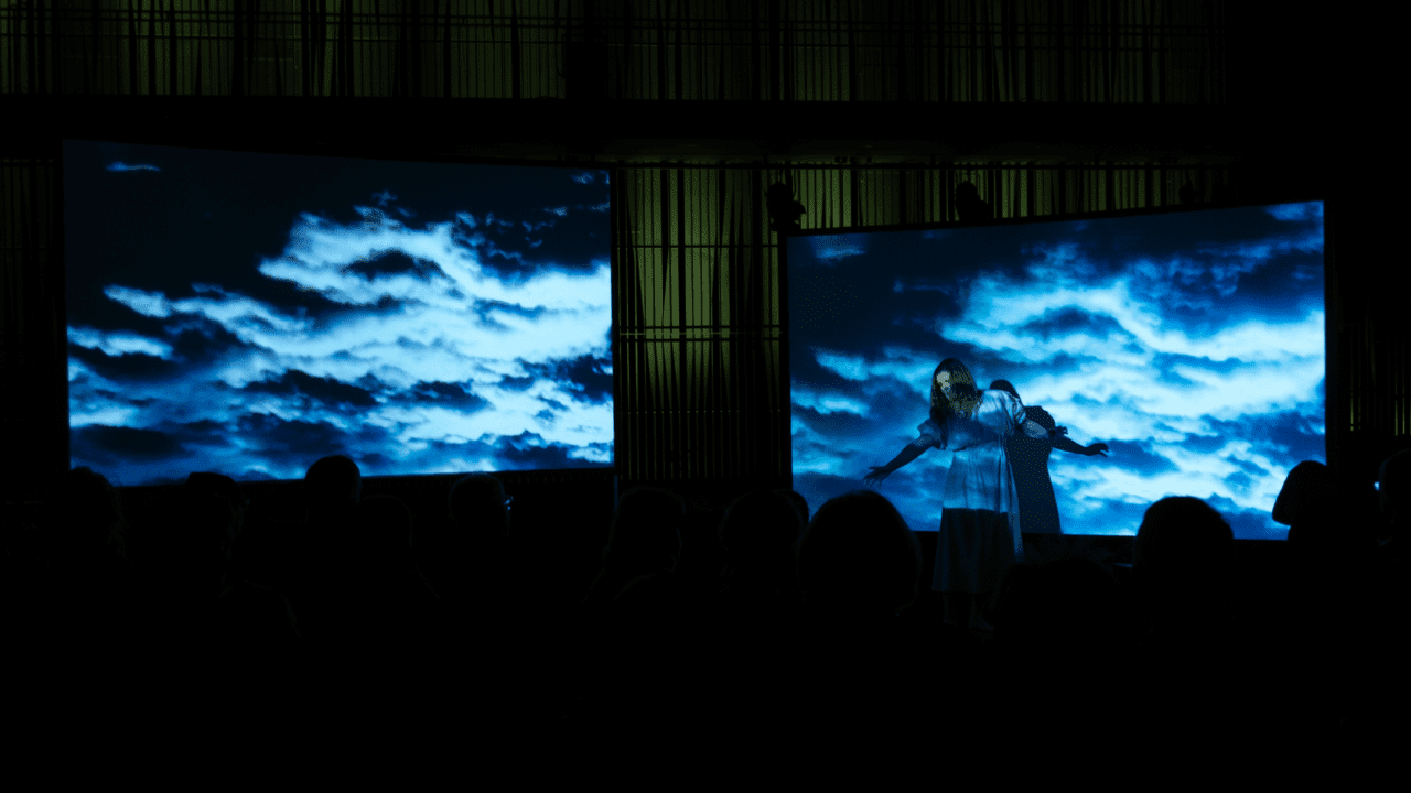 A photo from a performance and concert. A blue and dark background. A woman singing.