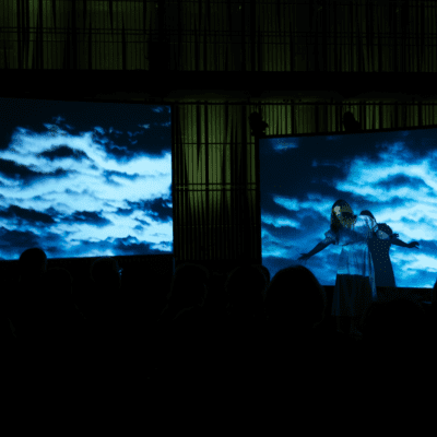 A photo from a performance and concert. A blue and dark background. A woman singing.