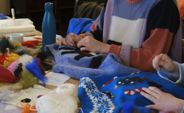 hands of two persons creating christmas sweaters from second hand sweaters, using yarn.