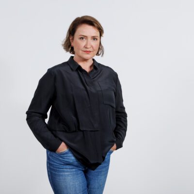Sunna standing infront of a white background with a black shirt and smiling to the camera