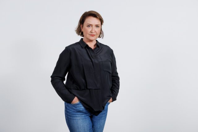 Sunna standing infront of a white background with a black shirt and smiling to the camera