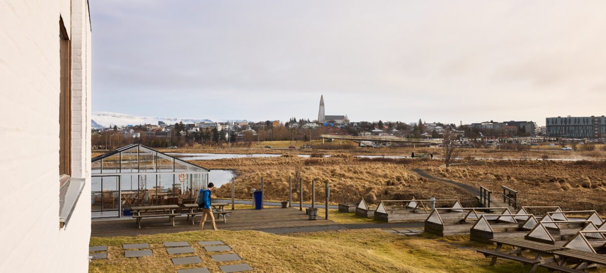 A man walks along a pathway at spring time. In the distance you see Hallgrimskirkja church and the sky. photographer is Jon Gudmundsson.