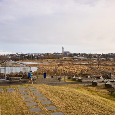A person in blue jacket walks along a pathway at spring time. In the distance you see Hallgrimskirkja church and the sky. photographer is Jon Gudmundsson.