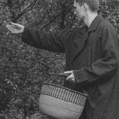 Sigmundur collecting leaves from a tree in black and white holding a basket