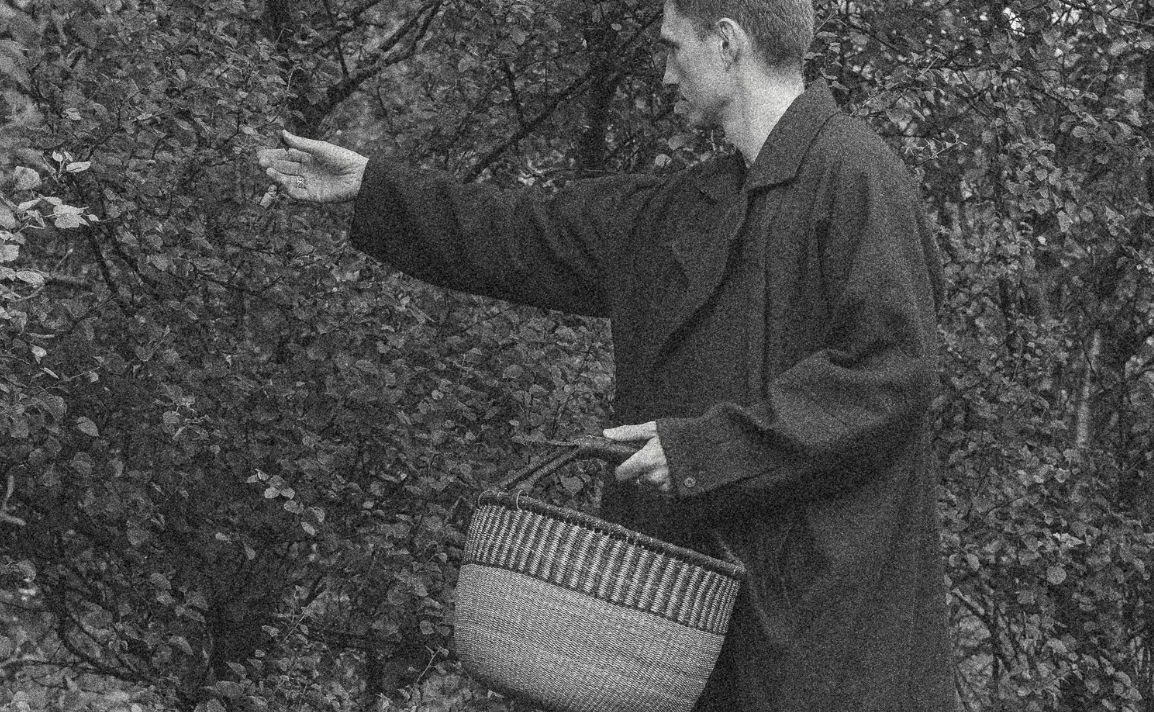 Sigmundur collecting leaves from a tree in black and white holding a basket