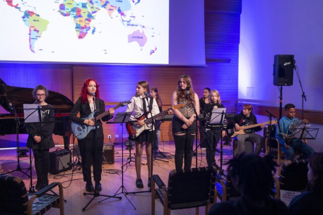 Teenagers stand on stage with instruments. Singing and performing. 