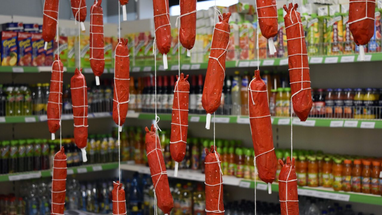 Red paper mache hotdogs hang from a ceiling in a grocery shop.