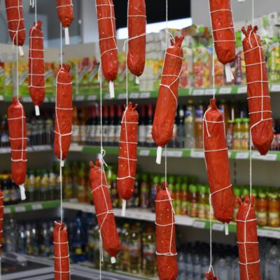 Red paper mache hotdogs hang from a ceiling in a grocery shop.