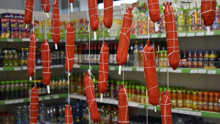 Red paper mache hotdogs hang from a ceiling in a grocery shop.