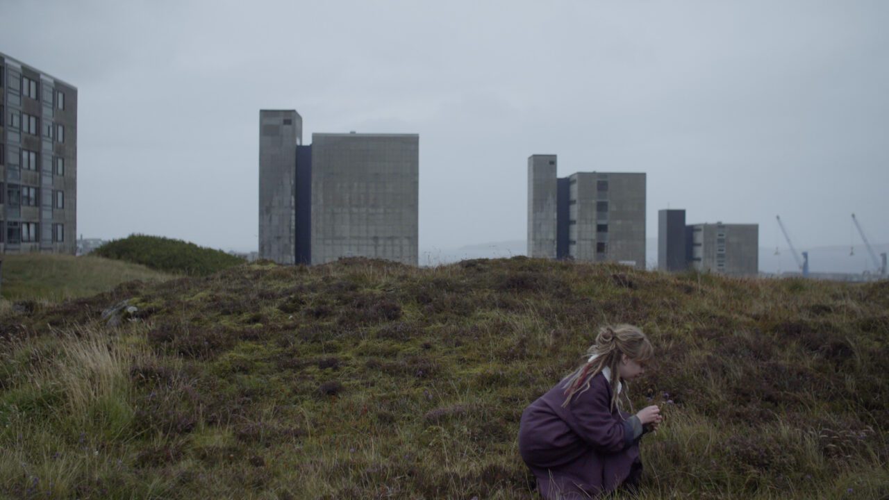A woman picks flowers, high buildings in the background. Photo credit: Rasmus Jensen