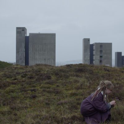 A woman picks flowers, high buildings in the background. Photo credit: Rasmus Jensen