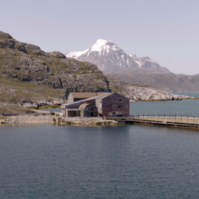 An abandoned building sits by a fjord. 
