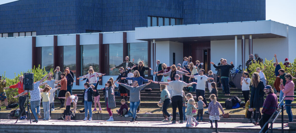 A group of people dancing in front of a white building with blue roof.