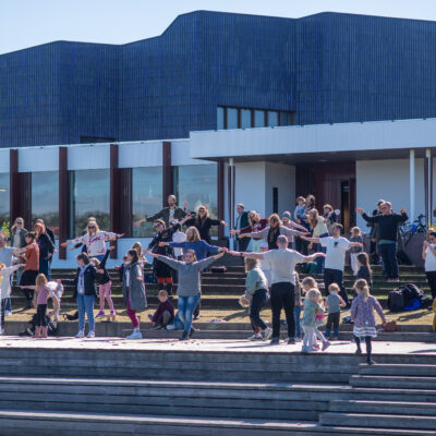 A group of people dancing in front of a white building with blue roof.