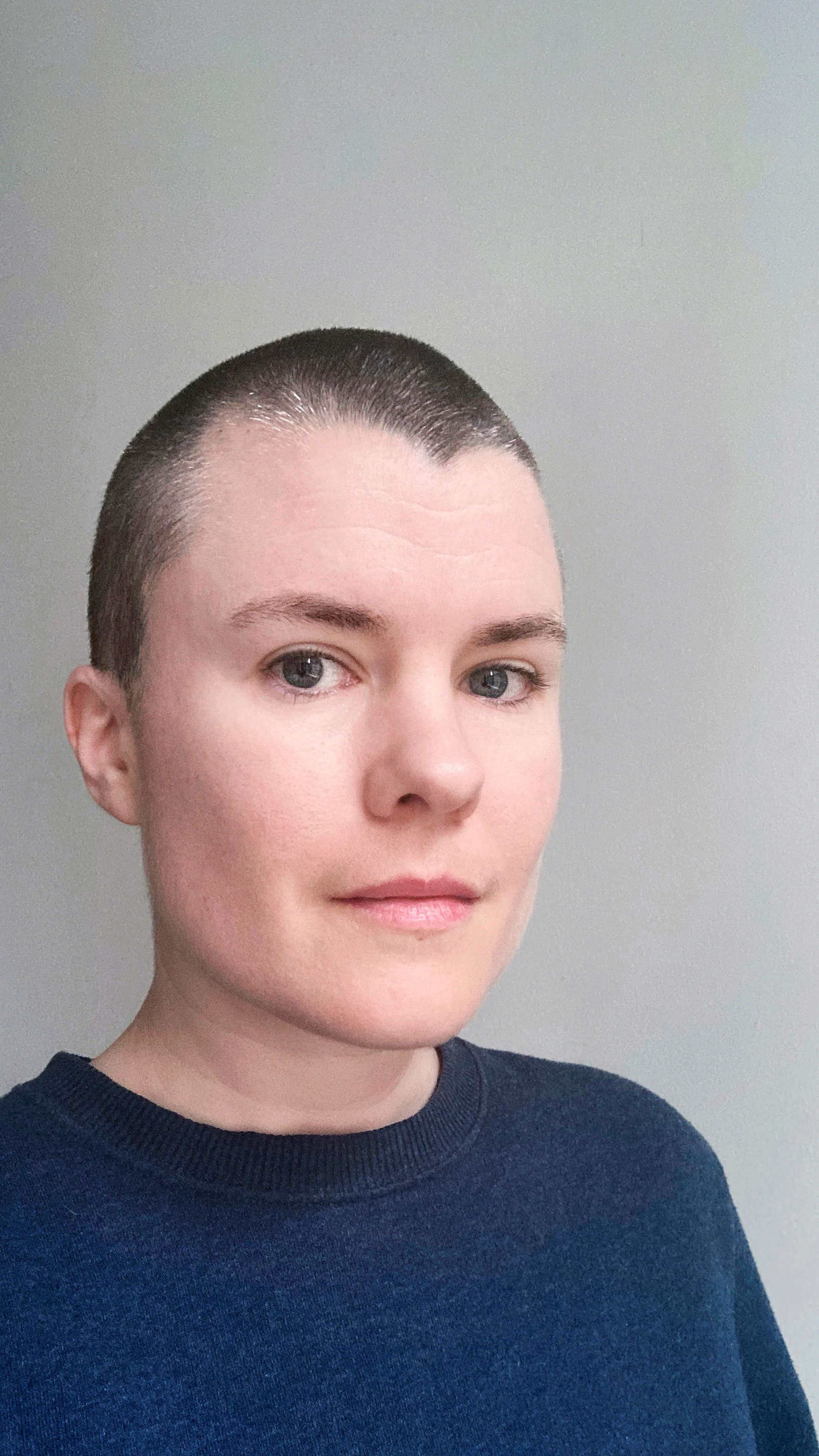 Portrait of a person. They wear a blue shirt and have short buzzed hair.
