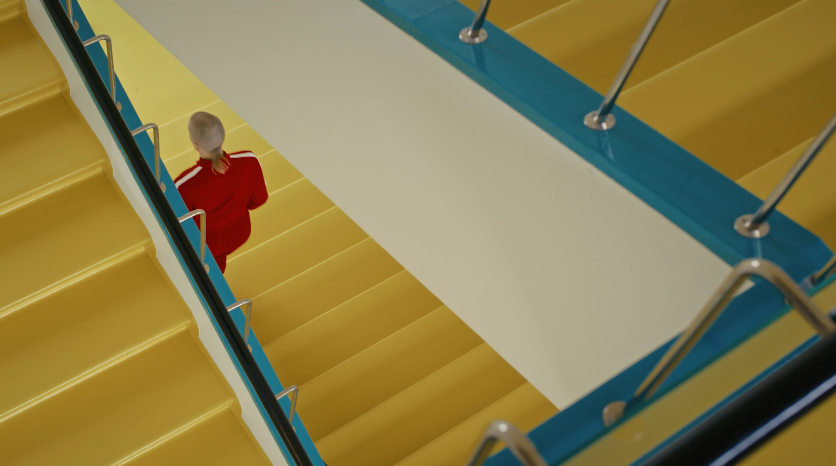 A person in a red tracksuit is seen running down a yellow staircase. The staircase has blue edges.